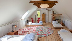 Een slaapkamer met een schuine kap, een groot raam, een bed met een kamerbreed tapijt en een houten garderobe.