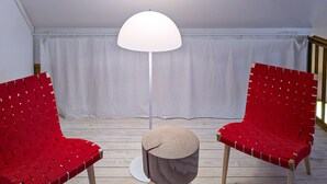 Een kamer met twee rode geweven stoelen, een ronde houten tafel en een witte vloer.