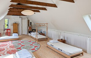 Ein Schlafzimmer im Loft-Stil mit schrägverdeckter Decke, zwei Einzelbetten, einem roten Sessel, einem Holzschrank und einem gemusterten Teppich.