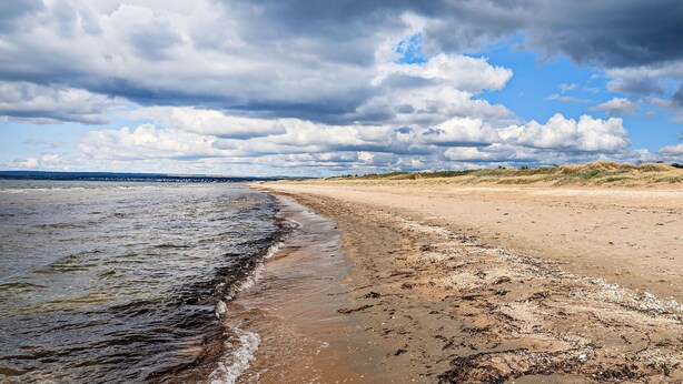 Een strand met een breed zandstrand, een rustige zee en een gedeeltelijk bewolkte lucht.