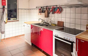 Eine Küche mit Geschirrspüler, Herd und Backofen, mit hängenden Küchenutensilien und einem Fenster über der Spüle.