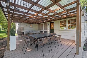 Eine überdachte Terrasse mit Holztisch und -stühlen, einer gepolsterten Sitzecke und Blick auf das Haus.