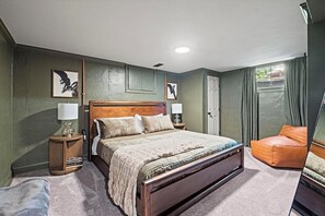 A bedroom with a large bed, two bedside tables, a nightstand, a chair, and a door. - The Mini Glenwood - A Cozy Ranch in Mission, KS (Mission)