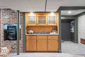 Basement wet bar with sink, cabinetry, and built-in beverage fridge set against exposed brick. A stylish lower-level entertaining space perfect for hosting, game nights, and group stays in this spacious 5-bedroom home. - The Mini Glenwood - A Cozy Ranch in Mission, KS (Mission)