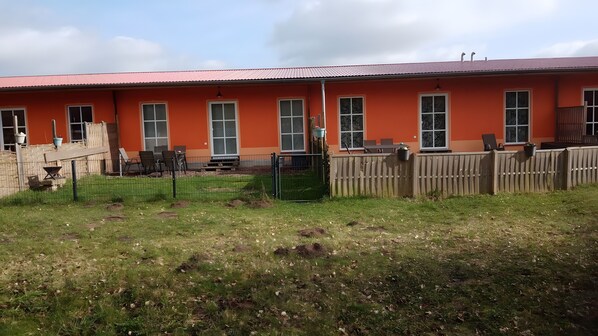 A building with a red roof and multiple windows, surrounded by a fenced area with grass and a wooden fence.