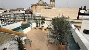 A rooftop terrace with potted plants, outdoor seating, and a view of historic buildings. - Alameda Grand Luxury (Seville)