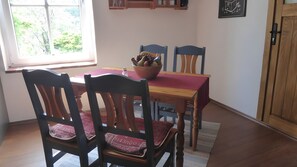 A dining area with a table, chairs, a bowl of fruit, and a window with a view of greenery. - Holiday Apartment for 2 People (45 m²) in Eggesin (Eggesin)