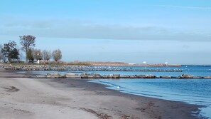Et kystlandskab med en sandstrand, en stenmolle og en fjerntliggende fyrtårn.