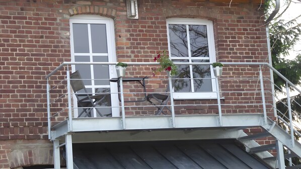 En murstensbygning med balkon, to vinduer og gelænder af metal.