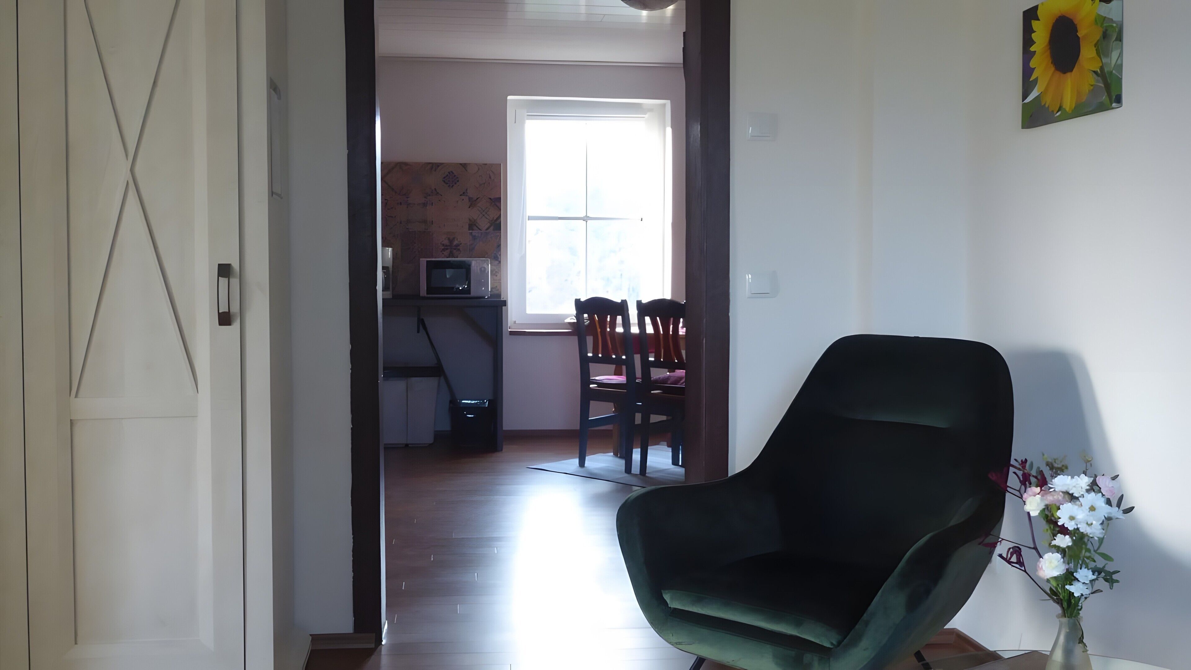 Une pièce avec un fauteuil vert, une table à manger avec des chaises, un four à micro-ondes et une fenêtre laissant entrer la lumière naturelle.