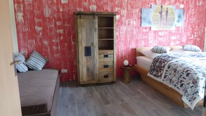 Een kamer met een bed, een kledingkast, een nachtkastje en een wand met een rood, structuurrijk patroon.