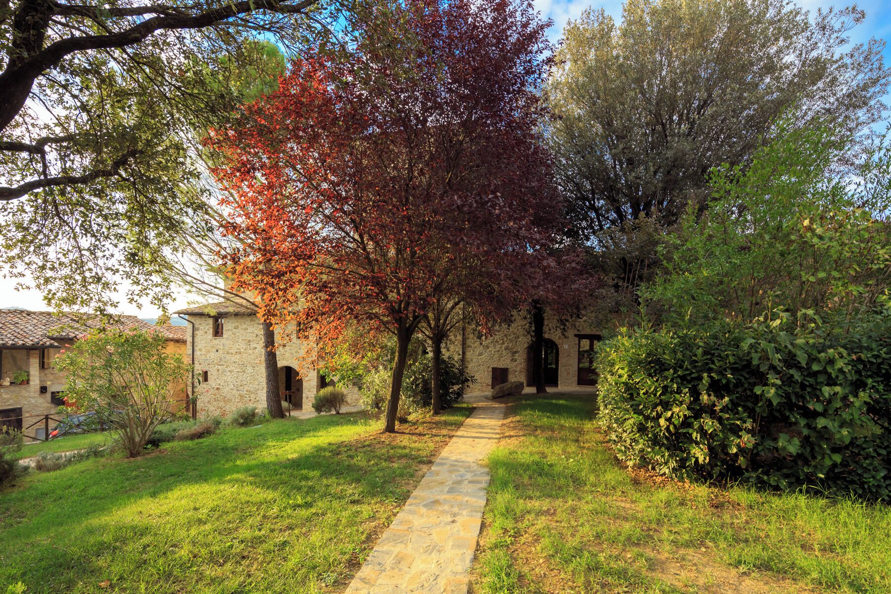 A stone pathway leading to a rustic stone building with a garden and trees.