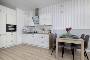 A modern kitchen with white cabinetry, a built-in oven, and a dining area with a wooden table and chairs. - Stylish Apartment with Balcony | Parking | Work Space (Katowice)