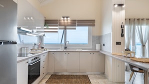 A modern kitchen with a large window, built-in oven, and a view of the sea. - Mario Luxury Seafront Penthouse with Jacuzzi – Casa di Mario, Kalyves, Crete (Kalives)