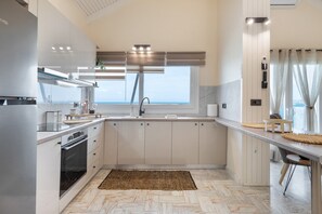 A modern kitchen with a large window, built-in oven, and a view of the sea. - Mario Luxury Seafront Penthouse with Jacuzzi (Kalives)