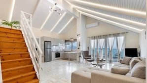 A spacious living area with a wooden staircase, a sofa, a dining table, and a kitchen in the background. - Mario Luxury Seafront Penthouse with Jacuzzi – Casa di Mario, Kalyves, Crete (Kalives)