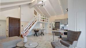 A spacious living area with a high ceiling, a staircase leading to an upper level, a dining area, and a kitchen. - Mario Luxury Seafront Penthouse with Jacuzzi – Casa di Mario, Kalyves, Crete (Kalives)