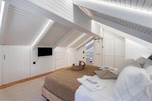 A bedroom with a large bed, a flat-screen TV mounted on the wall, and a wooden ceiling. - Mario Luxury Seafront Penthouse with Jacuzzi (Kalives)