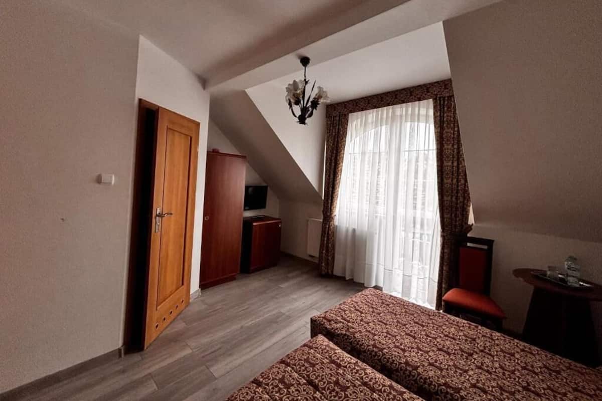 Un dormitorio con cama, escritorio, silla, armario, televisión y ventana con cortinas.