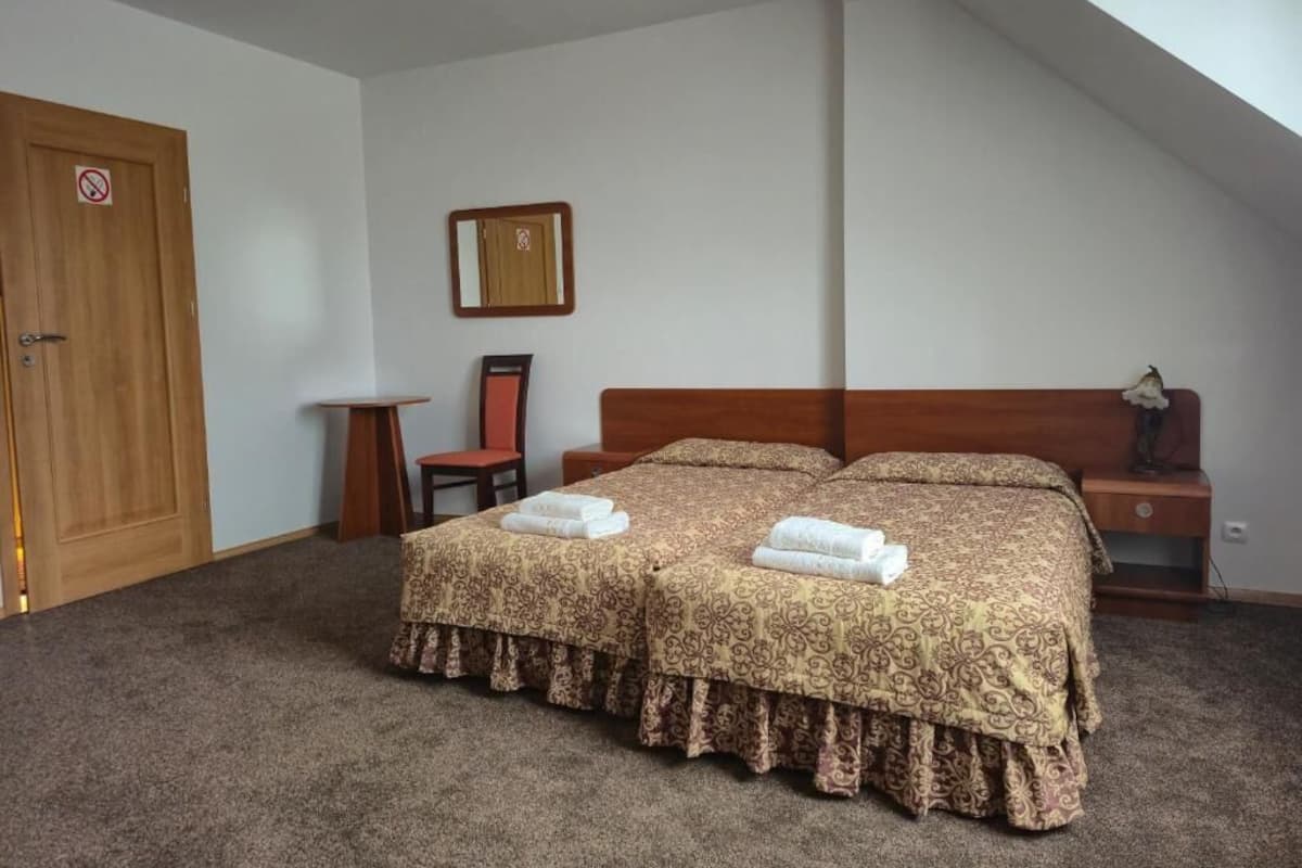 Un dormitorio con una cama grande, dos mesitas de noche, una puerta de madera y una pequeña mesa con una silla.