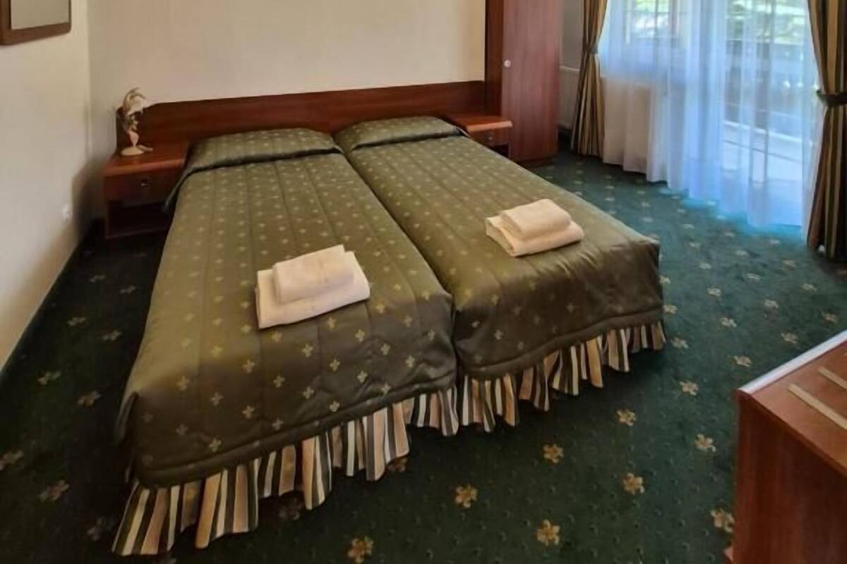 Una habitación con dos camas, vigas de madera en el techo, una lámpara de pared y una ventana con cortinas.