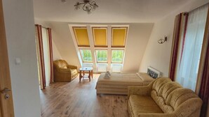 Una habitación con cama, sofá, sillón, una mesita y ventanas amplias con cortinas.