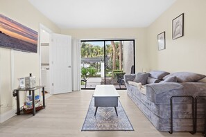 A living room with a sofa, a coffee table, and a view through a glass door to an outdoor area with plants. - Cozy Dr Phillips Condo Near Universal Studios (Orlando)