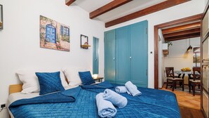 Ein Schlafzimmer mit einem großen Bett, blauer Bettwäsche, einem Gebäude-Gemälde und einem blauen Kleiderschrank.