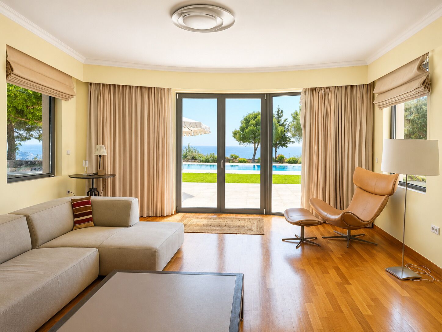 A modern living room with a sofa, a chair, a coffee table, and a view of a pool and greenery.