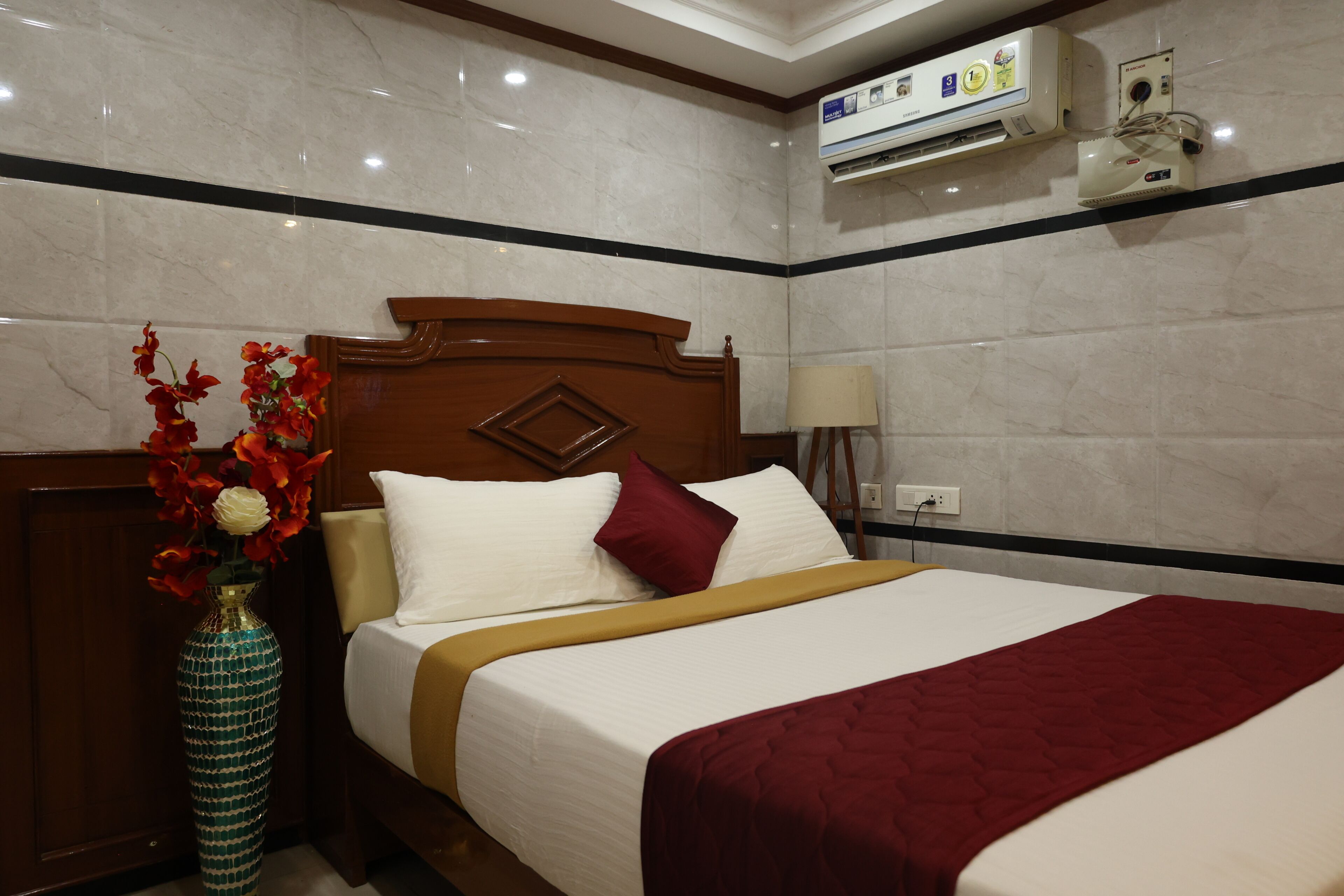 Une chambre d’hôtel avec un lit, un vase de fleurs, un appareil de climatisation et une lampe.