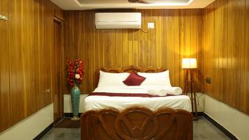 A hotel room with wooden panel walls, a bed with white linens, a vase with red flowers, and a standing lamp.