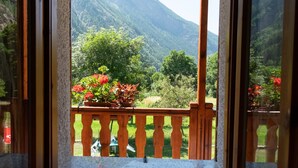 A room with a wooden balcony, a view of a mountainous landscape, and a potted plant with red flowers.