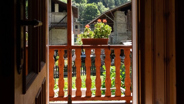 An open wooden door leading to a balcony with a view of a forested mountain.