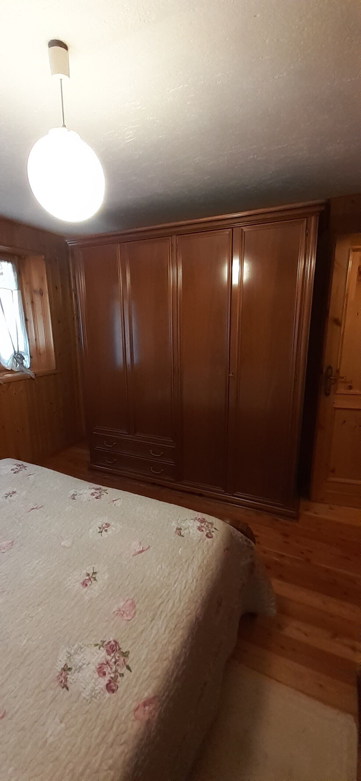 Una camera da letto con un armadio in legno, un letto con biancheria da letto a motivi floreali e un lampadario.