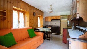 A wooden interior with a sofa, a dining table, and kitchen appliances.