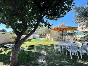 Un jardin avec une piscine, du mobilier d’extérieur et une pergola dotée d’un parasol.