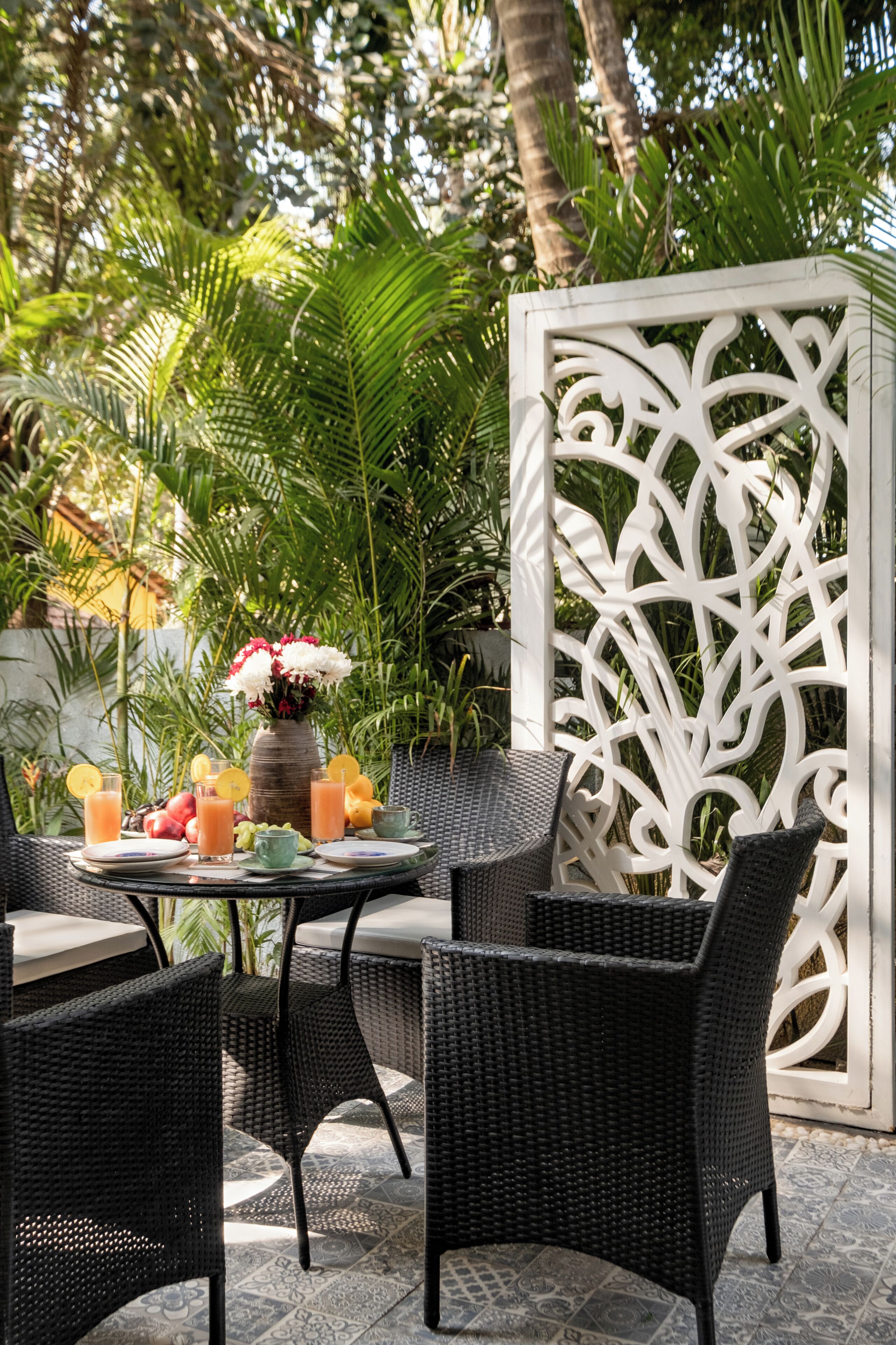 A patio with wicker furniture, a white decorative partition, and a table set with drinks and fruit.