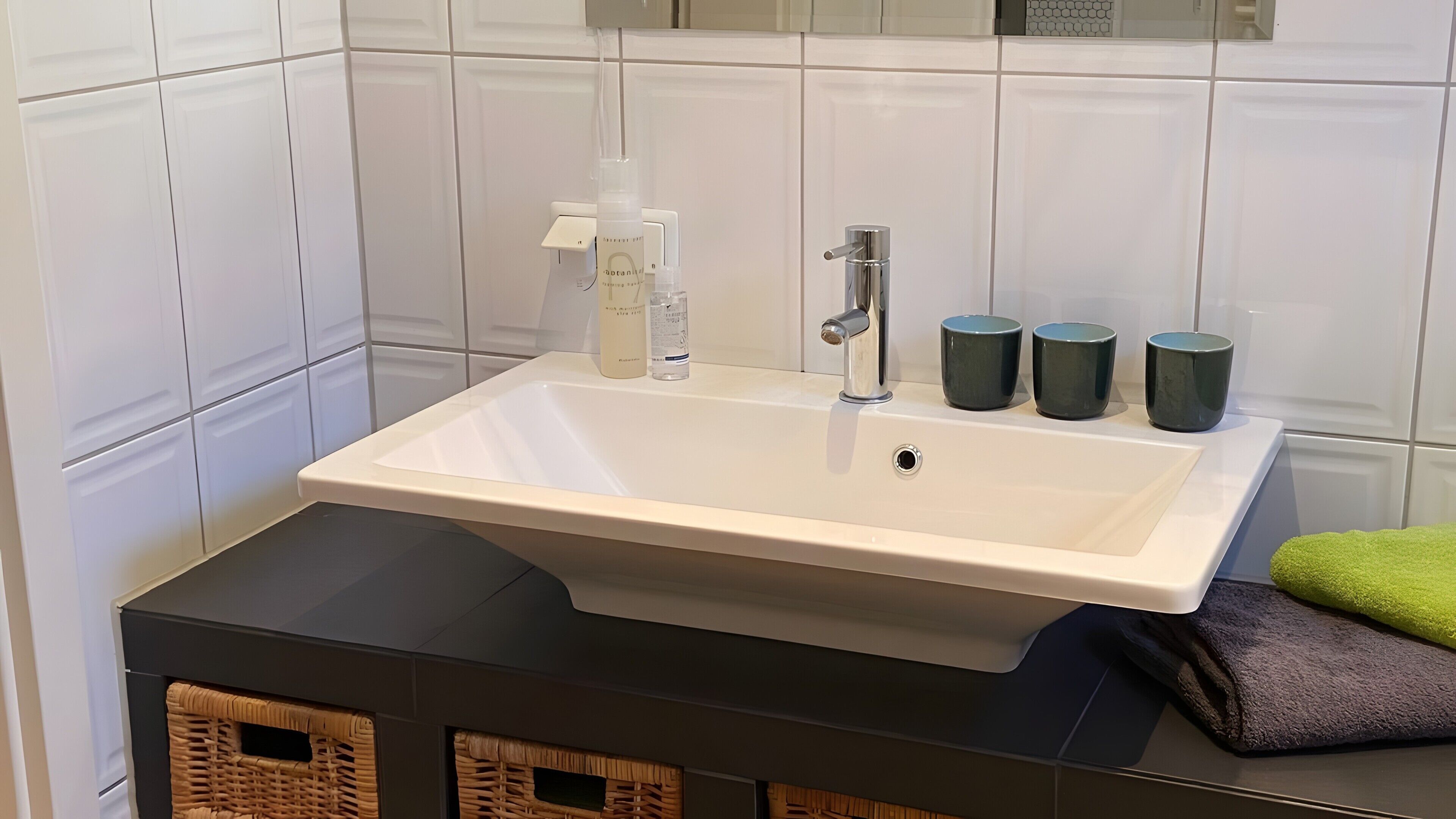 A bathroom with a white sink, a faucet, and three dark mugs on the counter.