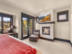 A bedroom with a large bed, a fireplace, a television, and a balcony with a view of the outside. - Main Street | 4BD ALL Ensuite | Hot Tub (Park City)