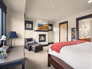 A bedroom with a bed, a fireplace, a TV mounted above it, a chair, and a desk with a lamp. - Main Street | 4BD ALL Ensuite | Hot Tub (Park City)