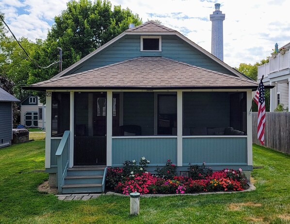 A small, single-story house with a porch, a chimney, and a garden with colorful flowers.