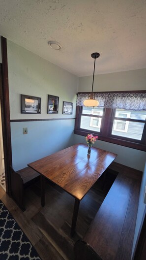A dining area with a wooden table, bench seating, a vase with flowers, and a window with patterned curtains.