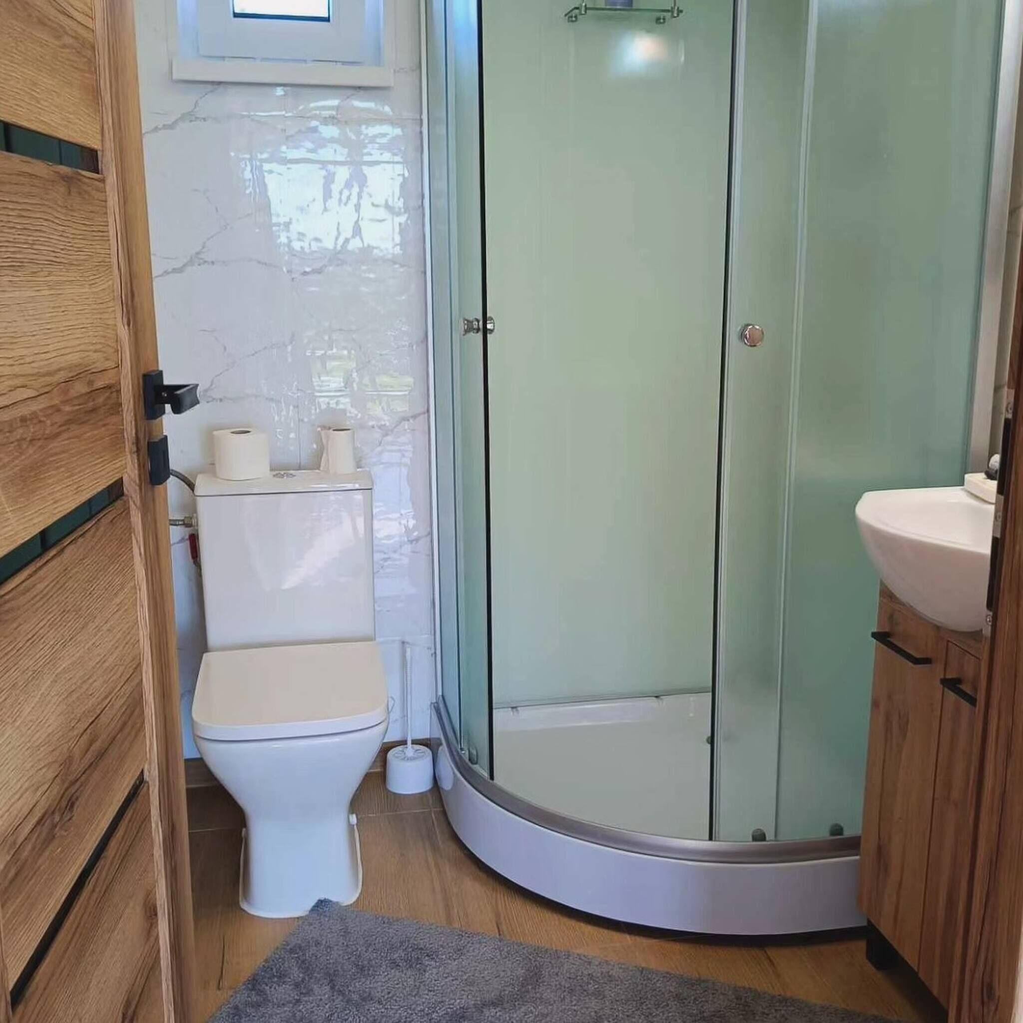 Un baño con inodoro, ducha con mampara de vidrio y lavamanos.