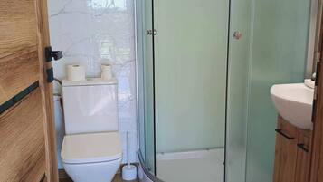 Un baño con inodoro, ducha con mampara de vidrio y lavamanos.