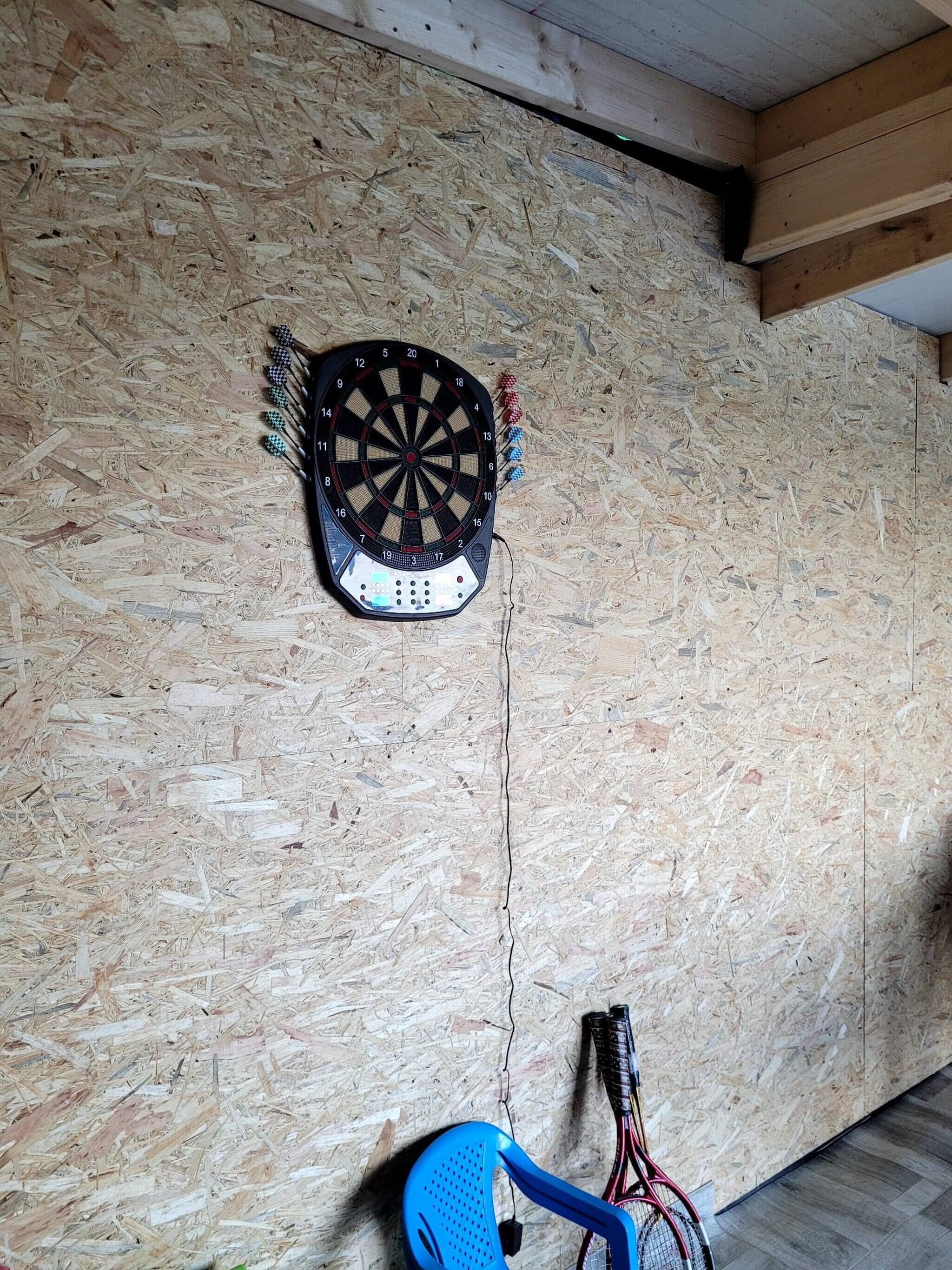 A dartboard mounted on a wooden wall with a blue chair and a guitar leaning against the wall.