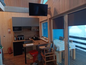A compact kitchen with a TV, a dining area with a table and chairs, and a view of the sea through a large window. - Domek nr 4 "błękitne Wzgórze" (gmina Brzuze)