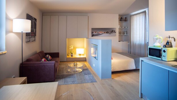 Een compacte hotelkamer met een bank, een klein tafeltje, een bed, een kitchenette en een tv aan de muur.