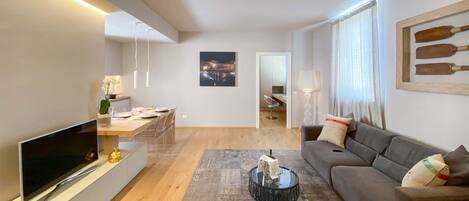 Una sala de estar moderna con un televisor de pantalla plana, un sofá, una mesa de centro y una zona de comedor con una silla y una mesa.
