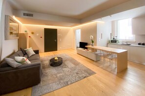 A modern living room with a sofa, a coffee table, and a kitchen area with a dining table and chairs. - Time to Be - COTONE  Luxury Apartments (Peschiera del Garda)