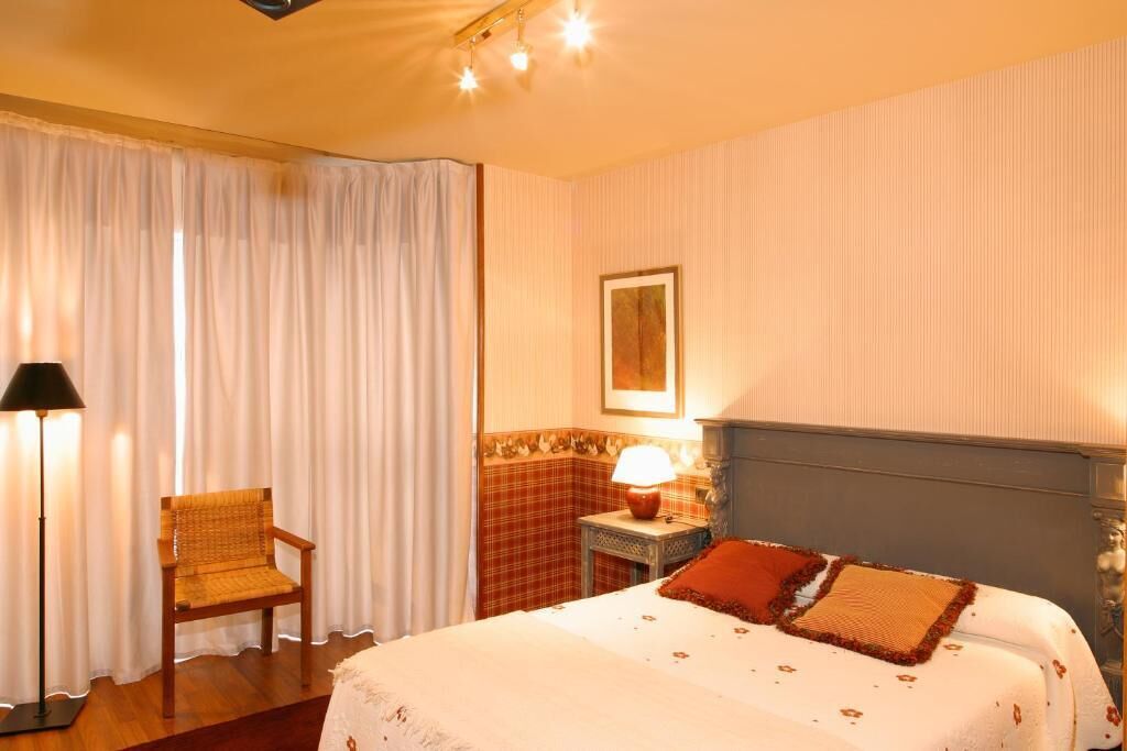 A hotel room with a bed, a chair, a lamp, and a painting on the wall.